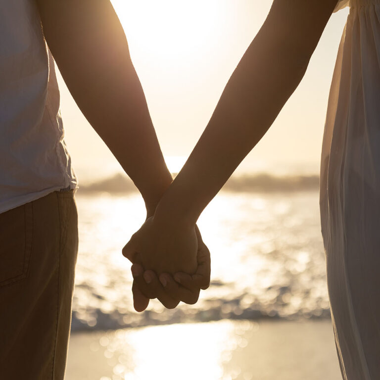 Mid section of couple standing together hand in hand on the beach