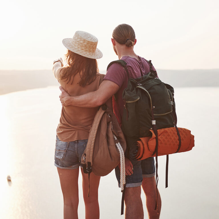 Two tourist male and woman with backpacks stand to the top of the mountain and enjoying sunrise. Travel lifestyle adventure vacations concept.